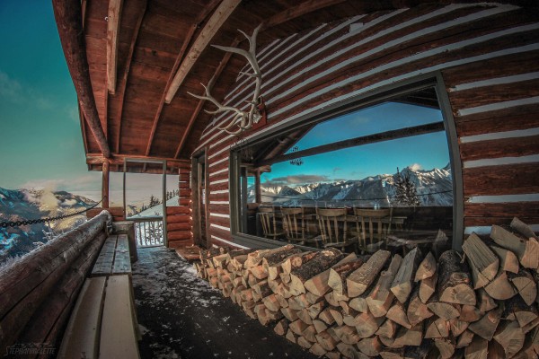 The historic Elkhorn Cabin located at Panorama Mountain Resort surrounded by snow the a view of the mountains reflected in the window.