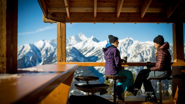 Two women drink coffee and look at the vast view of the mountains from the deck of the Elkhorn Cabin at Panorama Mountain Resort
